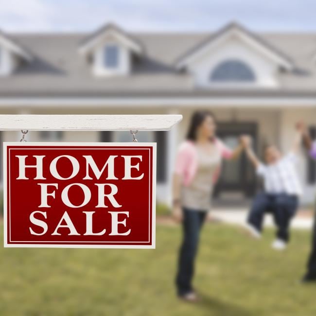 "Home for sale" sign in the foreground, a family of three standing in front of their new house in the background.